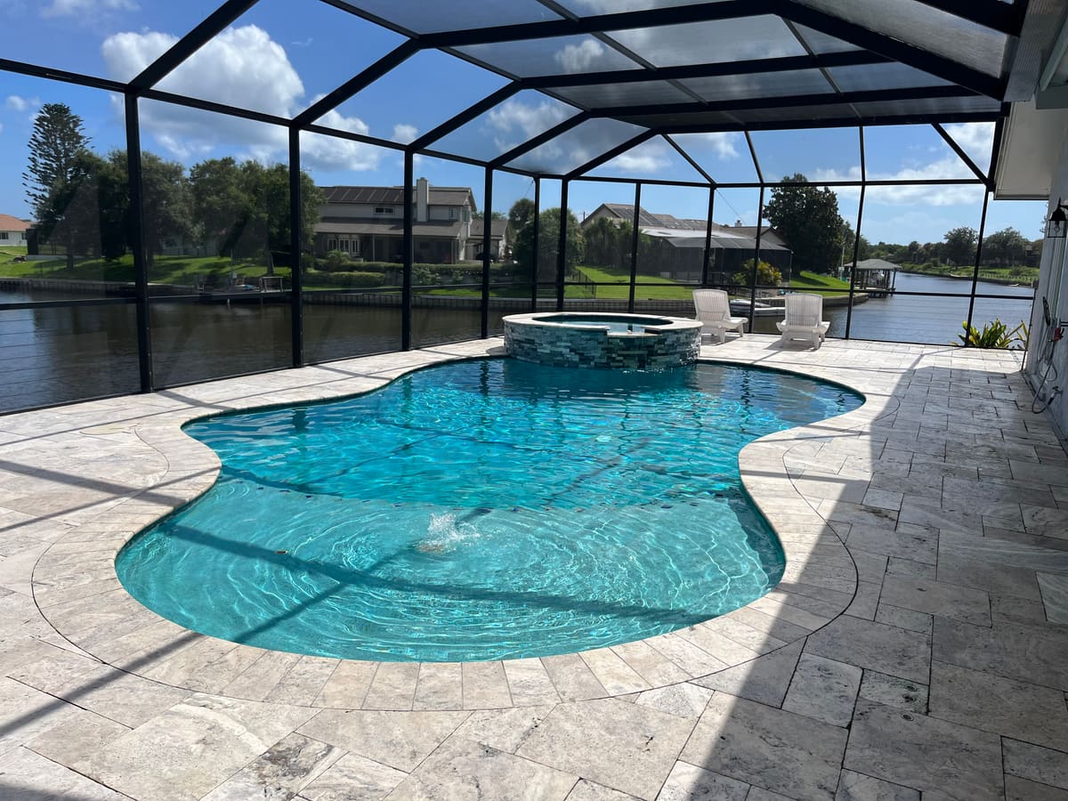 Finished lagoon-shape pool with raised spa on a screened, canal-view lanai — a recent TruBlue Pools project
